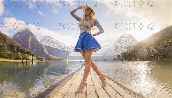 Woman in denim skirt and sandals standing on a wooden road by a lake with mountains in the background, daytime, AI generated, AI generated