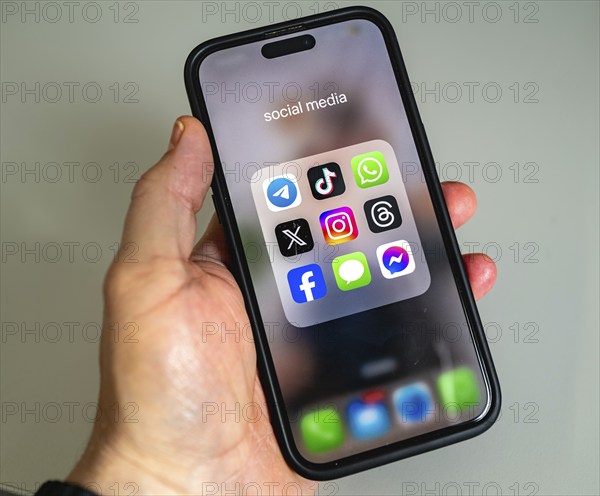 A smartphone is held in the hand and shows app icons, display on a screen, WhatsApp, Tik Tok, X, Facebook and Messages app, instant messenger service, social networks