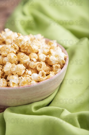 Popcorn with caramel in ceramic bowl on brown concrete background and green textile. Side view, close up, selective focus