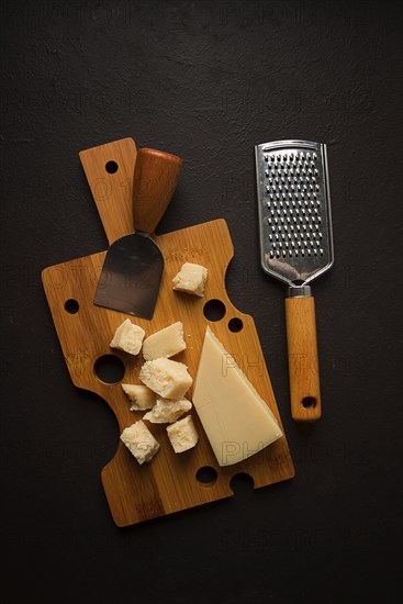 Hard cheese, parmesan, on a cutting board, cheese knife, grater, top view, no people