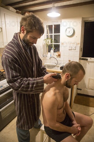 Young man shaving his brother's head home haircut in kitchen, UK, model released