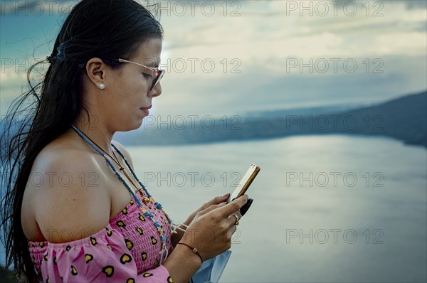 Beautiful girl in glasses checking mobile phone. Side view of young woman checking smartphone outdoors