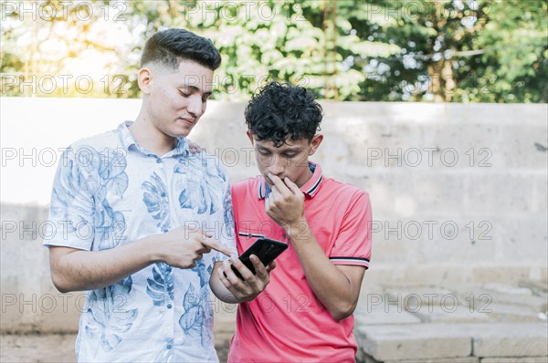 A guy showing his cell phone to another guy, Teenager explaining with his cell phone to another guy, A young man explaining with his cell phone to a young man