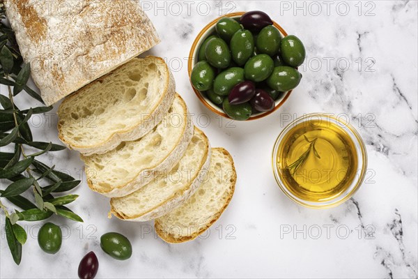 Appetizer, sliced ciabatta bread, with olive oil, green olives, Chalkidiki olives, classic Green green olive, on a marble table, top view, no people