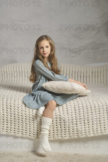 A serene image of a girl wearing a mint dress, sitting on a knitted blanket with a pillow. The soft textures and neutral tones convey a sense of comfort and tranquility