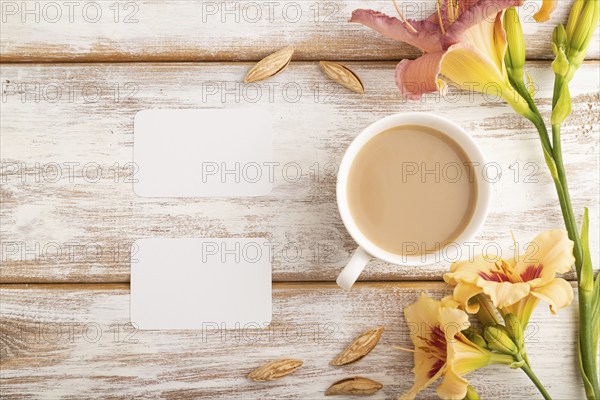 White paper business card mockup with orange day-lily flower and cup of coffee on white wooden background. Blank, top view, flat lay, copy space, still life. spring concept