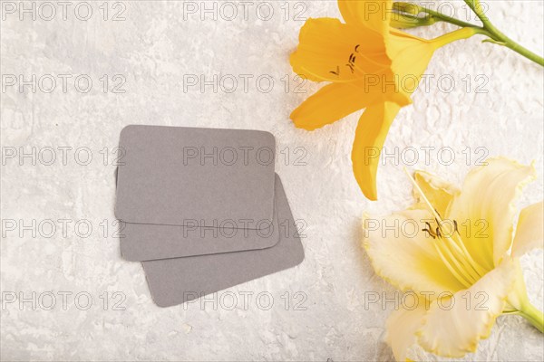 Gray paper business card mockup with orange day-lily flower on gray concrete background. Blank, top view, copy space, still life. spring concept