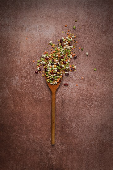 Wooden spoon, with an assortment of legumes, beans, peas, top view, on a brown background