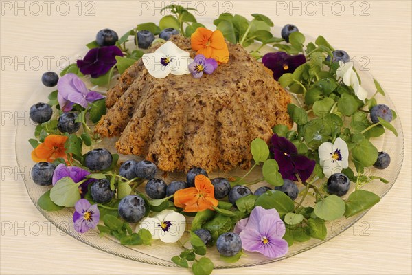 Vegetarian cuisine, chestnut roast, chestnut cake, chestnut roast, chestnut cake with hazelnuts, chestnut cake, savoury, vegan, salty, baked, from the oven, healthy, main course, glass plate, new cuisine, decoration with pansies, violet (Viola), blueberries (Vaccinium), blueberries, food photography, studio, Germany, Europe