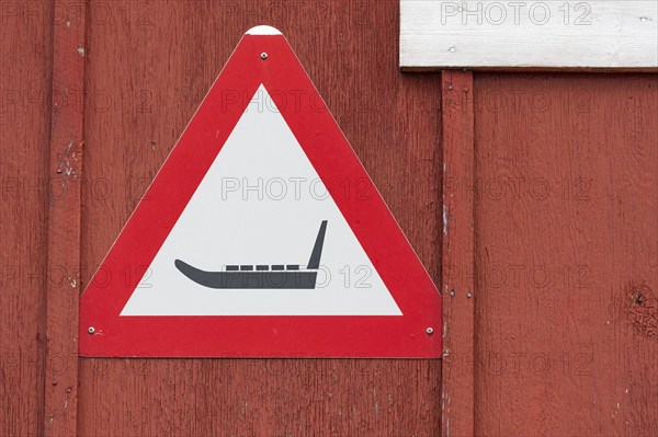 Triangular warning sign with sledge symbol on a red wooden wall, remote Arctic Inuit settlement Ittoqqortoormiit, Scoresbysund or Scoresby Sund or Greenlandic Kangertittivaq, East Greenland, Greenland, North America