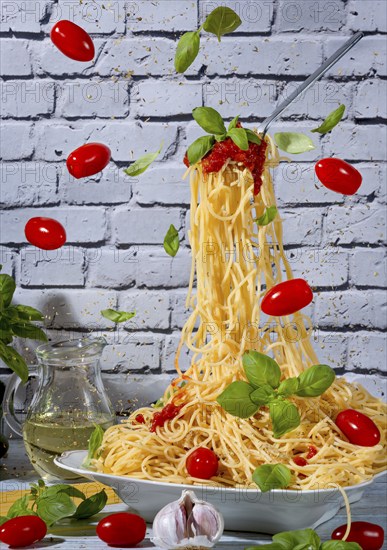 Spaghetti in a bowl and on a floating fork surrounded by tomatoes, basil and garlic