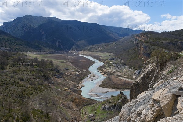 A river meanders through a wide valley surrounded by green hills and rocky mountains under a partly cloudy sky, Noguera Ribagorçana Mont-rebei Natural Park, Montsec mountain range, Noguera Ribagorçana river, Lleida province, Catalonia, Aragon, Spain, Europe