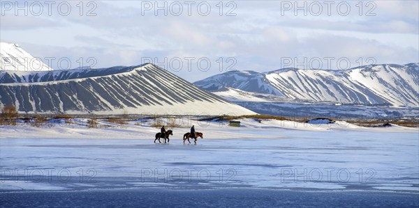 Two riders on horses on a partly frozen ice surface in a snow-covered winter landscape, volcanoes in the background, fire and ice, Myvtn, Iceland, Europe