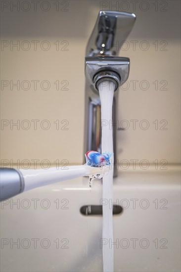 A bathroom tap is running while a toothbrush is held under the running water, symbolic image of water consumption