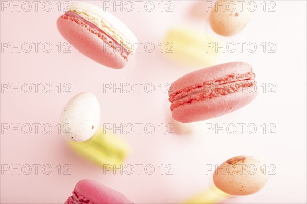 Multicolored flying macaroons and chocolate eggs frozen in the air on blurred pink background. top view, flat lay, close up. Breakfast, morning, concept