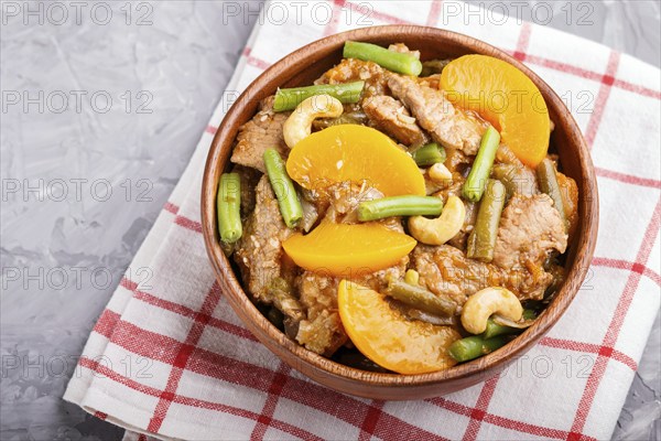 Fried pork with peaches, cashew and green beans in a wooden bowl on a gray concrete background. Top view, close up, chinese cuisine