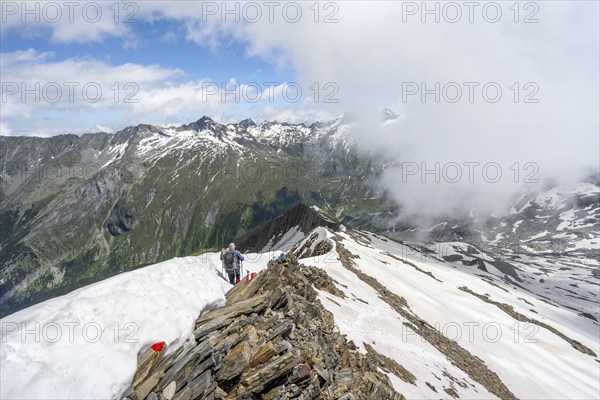 Mountaineer on a rocky ridge with snow, descent from the summit of Schönbichler Horn, view of snow-covered mountain peaks and valley Zemmgrund, Berliner Höhenweg, Zillertal Alps, Tyrol, Austria, Europe