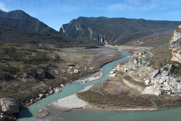 A clear jade river flows through a wide valley, surrounded by dramatic cliffs and wooded mountains under a blue sky, Noguera Ribagorçana Mont-rebei Natural Park, Montsec mountain range, Noguera Ribagorçana river, Lleida province, Catalonia, Aragon, Spain, Europe