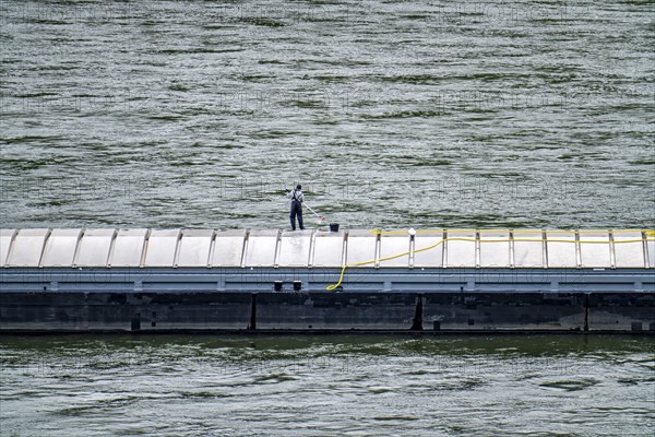 Inland waterway vessel, freighter, with closed cargo hatches, employee cleans the deck with water and scrubbing brush, on the Rhine, Rhineland-Palatinate, Germany, Europe