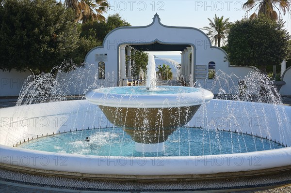 Large Mediterranean-style fountain with bubbling water and palm trees in the background under a clear sky, thermal springs, thermal baths, thermal baths of Kallithea, Kallithea, Rhodes, Dodecanese, Greek Islands, Greece, Europe