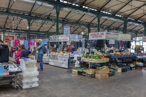 Busy indoor market filled with vegetable and clothing stalls and people, Belfast