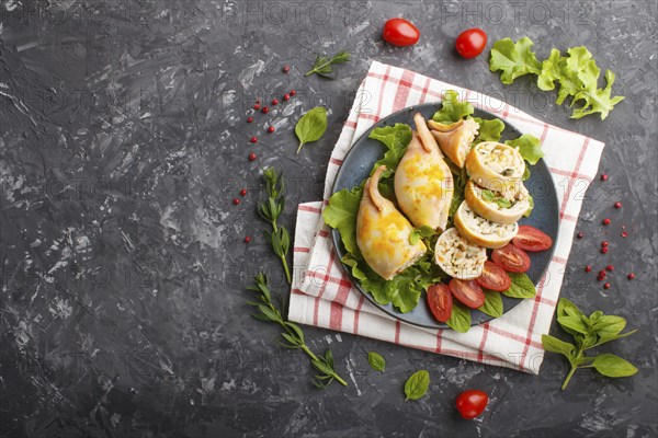 Stuffed baked squid with greens on a blue ceramic plate on a black concrete background, top view, flat lay, copy space