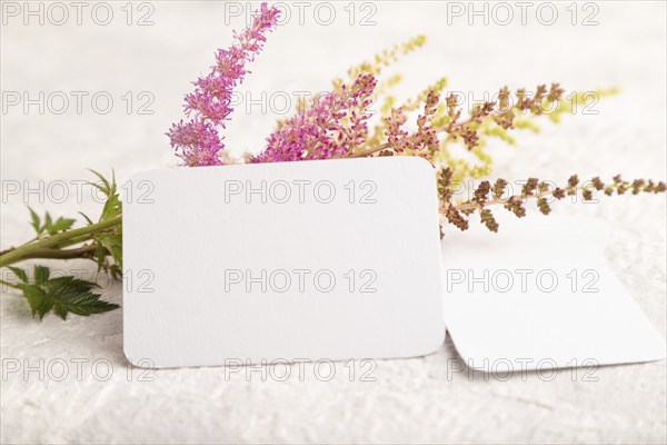 White paper business card mockup with purple astilbe flowers on gray concrete background. Blank, side view, copy space, still life. spring concept