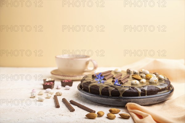 Homemade chocolate brownie cake with caramel cream and almonds with cup of coffee on a white and orange background and orange textile. Side view, copy space, selective focus