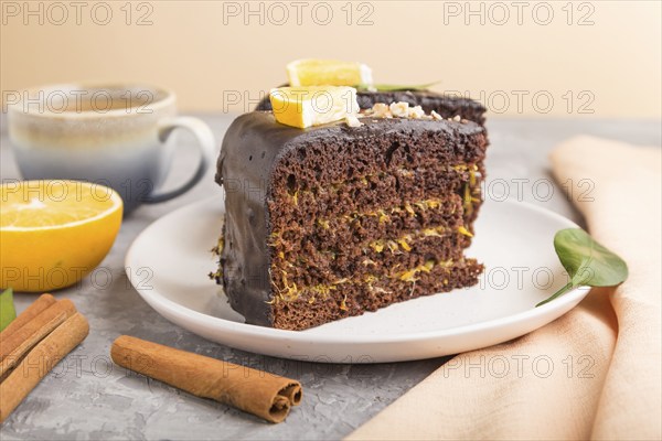 Homemade chocolate cake with orange and cinnamon with cup of coffee on a gray concrete background with orange textile. side view, close up, selective focus