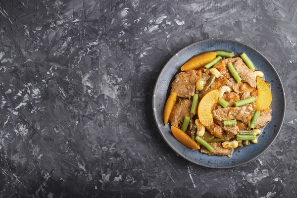 Fried pork with peaches, cashew and green beans on a black concrete background. Top view, copy space, flat lay. chinese cuisine