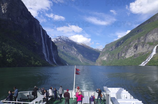 People enjoy the journey through a picturesque fjord with mountains, waterfalls and blue skies, ferry trip Geiranger to Hellesylt, Fjordland, Norway, Europe