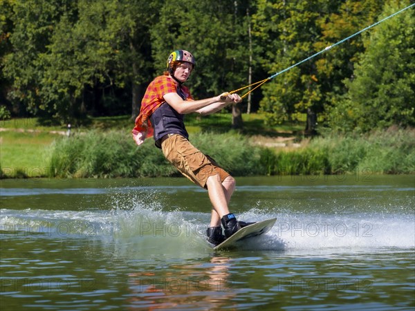 Young casual man with flapping shirt on wakeboard in lake, water ski and wakepark, Stráž pod Ralskem, Czech Republic, Europe