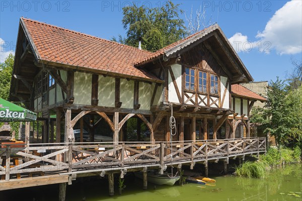 Half-timbered house with terrace by the water, surrounded by green nature and blue sky, Restaurant Tawerna, Ostroda, Osterode in East Prussia, Warminsko-Mazurskie, Poland, Europe