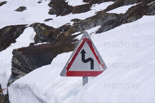 Traffic sign on a snow-covered mountain road indicating a sharp bend, June, Geiranger, Fjordland, Norway, Europe