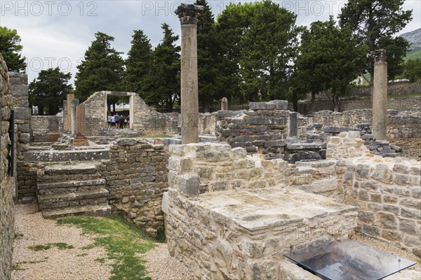 Old stone structures and columns plus tourists at ancient 3rd century Roman ruins of Salona near Solin in late summer, Croatia, Europe