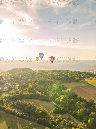 Hot air balloons hovering over farmland and forest in a hilly landscape at sunset, Calw, Black Forest, Germany, Europe