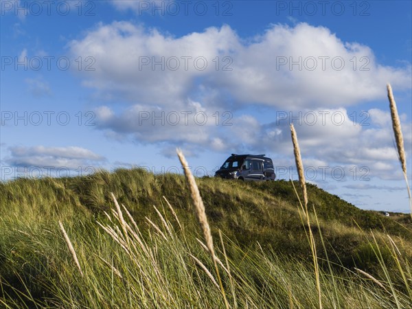 A campervan stands on a grassy dune under a blue sky with clouds, North Sea, Jutland, Denmark, Europe