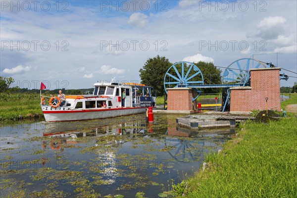 A boat passes a lock in a green landscape in sunny weather, ship Zefir, manoeuvrable wheels in the lower pillar for aligning the rope for the rail cars, Upland Canal, Warminsko-Mazurskie, Poland, Europe