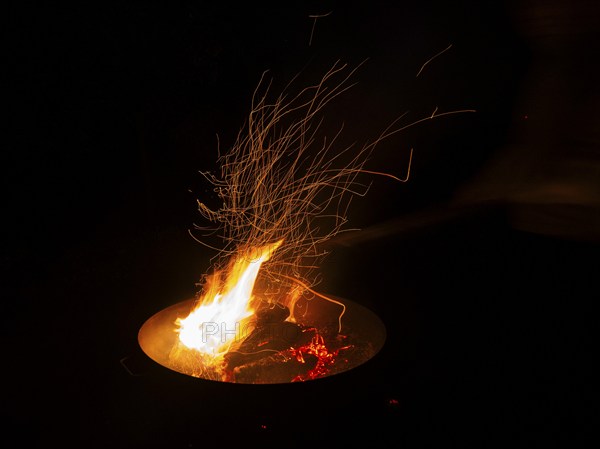 Garden Barbecue Pan, filled with burning wood, creating flames and sparks against the nighttime surroundings, North Hesse, Germany, Europe