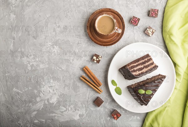 Homemade chocolate cake with milk cream and a cup of coffee on a gray concrete background with green textile. top view, flat lay, copy space