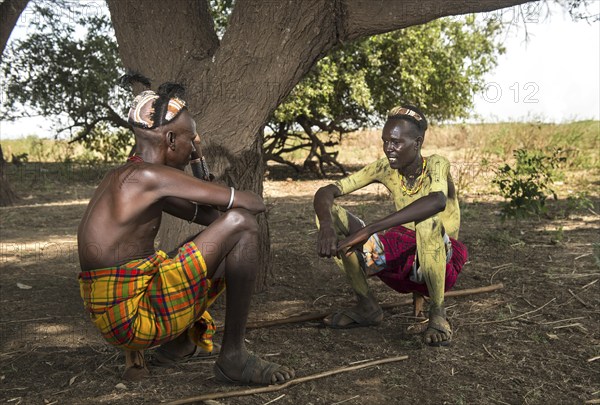 Two young men with traditional clay headdresses sitting on wooden headrests converted into stools, Dassanetsch ethnic group, Southern Omo Valley, Ethiopia, Africa