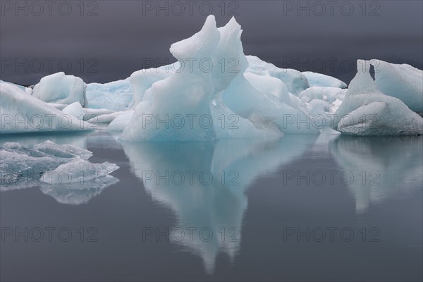 Symmetrical ice structures reflected in the calm water, grey sky, Jökulsárlón or Jökulsarlon glacier lagoon, South Iceland, Iceland, Europe