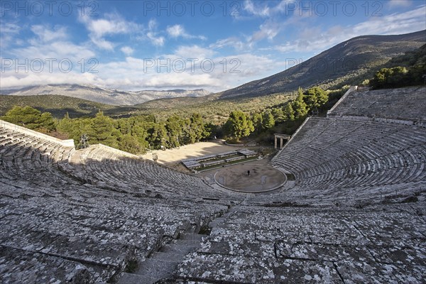 Panoramic view of an ancient amphitheatre against a mountain backdrop under a partly cloudy sky, Ancient Amphitheatre, Epidaurus, Peloponnese, Greece, Europe