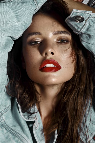 Beautiful sexy girl with bright makeup, red lips, wet hair in a denim jacket. Beauty face. Photo taken in studio