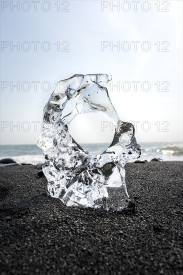 Ice, piece of ice with hole on black sand beach, on black lava beach Diamond Beach, Southeast Iceland, Iceland, Europe