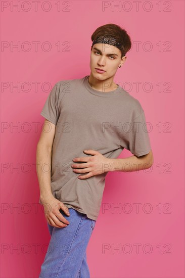 Studio portrait of young man in olive t-shirt, jeans and bandana on head over pink background