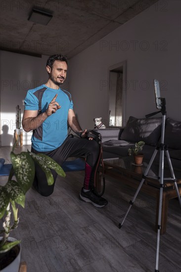 Filming online classes with confident professional fitness trainer. Exercising at home. Young sports man blogger recording video on phone camera