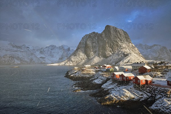 Hamnoy fishing village on Lofoten Islands, Norway with red rorbu houses. With falling snow blizzard in winter and rainbow