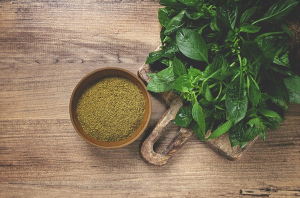 Ground green basil, in a ceramic bowl, with a bouquet of fresh green basil, on the table, top view, no people