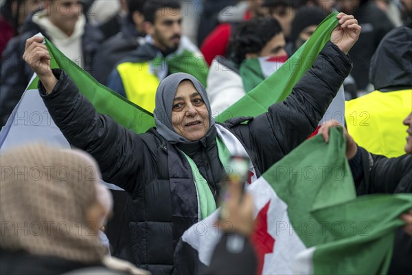 Syrian woman celebrate the end of the Assad regime after the change of power in Syria at a rally on the square in front of the main railway station in Duisburg, North Rhine-Westphalia, Germany, Europe